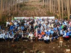 両脇に木々が生え、中央の木々が伐採された開けた山の斜面で参加者達が集まって集合写真を撮っている写真