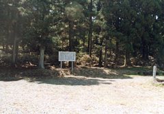 木々に覆われた林の手前の広場に説明の看板が立っている寺跡の写真