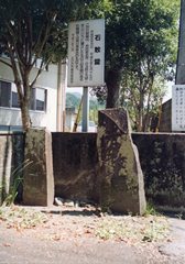 塀の後ろに立て看板が立っている、高さの違う2つの石敢当の写真