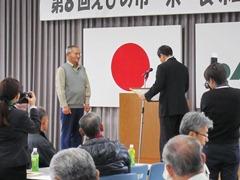 舞台上で表彰される男性と座ってみている参加者達の写真