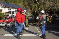 赤色フルフェイスのヘルメットを被った人たちが横一列に整列し、白いヘルメットを被った男性の話を聞いている写真