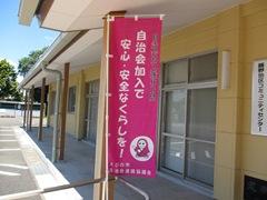 黄色い建物の横にたてられた、自治会加入で安心・安全なくらし!をと書かれたピンクの旗の写真