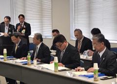 長机の席に座り資料を見ている数名の男性と資料を見ながらマイクで話をしている2名の男性の写真