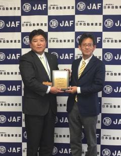 JAFと書かれた背景に表彰盾を一緒に持っている市長と1名の男性の写真
