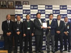 JAFと書かれた背景に表彰盾を持っている市長と1名の男性、その周りに立っている数名の男性の写真