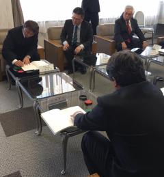 椅子に座りローテーブルに置いてある紙に印鑑を押している2名の男性とその姿を座って見ている2名の男性の写真