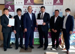 6名のうち、左端に立つ市長と真ん中の男性が白い紙を持っている集合写真