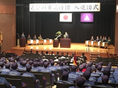 えびの市消防団入隊団式と幕がかかった舞台が奥にあり、手前には式の参加者達の後ろ姿が写っている写真