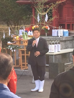 後ろにはお供え物が置かれていて、手前には長靴を履いてマイクで話をする市長が写っている写真
