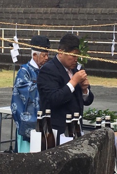 奥には神主、手前には玉ぐしを持って顔に近づけてお祈りをする市長が写っている写真