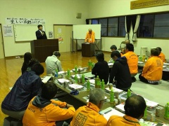 テーブルの上には飲み物や資料が置かれ、参加者達が座って市長の話を聞いている定例会の写真