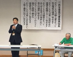 壁には民生委員児童委員信条が貼られており、手前で市長がマイクを持って話をしている写真
