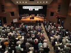奥には舞台、手前には参加者達が観客席で話を聞いている様子が写っている写真
