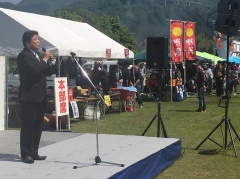 横に本部席のテントがある舞台でスーツを着た市長が話をしている写真