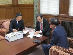 テーブル上に置かれた要望書を見ている3人の男性の写真