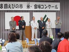 舞台上で立っている6名の男性と座って聞く参加者達の写真