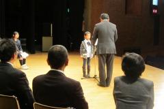 舞台上で男性から表彰される男の子の写真