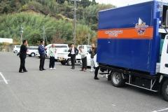 駐車場に停まっている青色のトラックの後方に立っている数名の写真