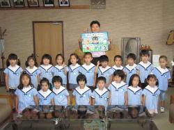 市内幼稚園の園児と、絵が描かれたメッセージを持つ市長が集合し記念撮影をしている写真