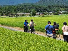 田園風景の中eバイクに乗り撮影する市長と戸波さん