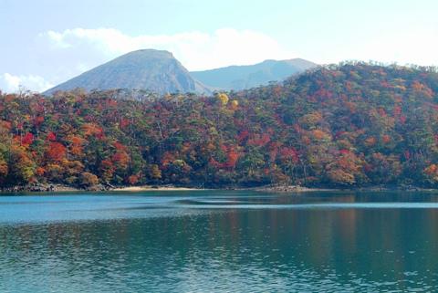 六観音御池の周りの木々が紅葉し、後方に韓国岳が見えている写真