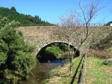 石造りのアーチ型をした太鼓橋の下が水路になっており、周りに木々が植えられている写真