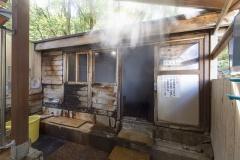 木造の天然蒸し風呂の入り口が開いており、蒸気が出ている写真