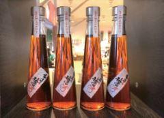 茜色をした明月梅酒(ツユアカネ)の瓶が4本並べて置かれている写真