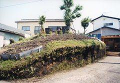 周囲に民家が建っているなか、中央に土が盛られている古墳の写真