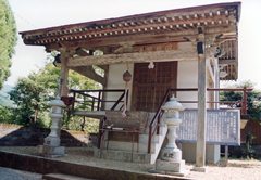 手前両側に2つの灯篭がある小さな神殿の右側に説明看板が設置されている剣神社の写真