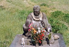 首に輪っかをかけている、花が供えられが田の神像をアップで撮影した写真