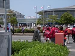 奥にはドーム状の建物があり、赤いおそろいの上着を着た参加者たちが会場に向かって歩いている写真