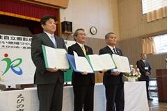 えびの市長、小林市長、関係者の男性の3人が協定書を見せながら並んで立っている写真