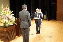 代表の男性が舞台上でえびの市長と向かい合わせに立って話をしている写真