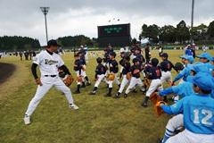 野球のユニフォームを着た男性が子供たちに野球を教えている写真