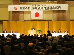 奥には日本国旗と祝電波の日・情報通信月間記念式典と幕が掲げられ、手前には椅子に座っている参加者たちを後ろから写した写真