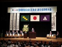 頭上に宮崎県自治会（区長会）連合会研修会と書かれた幕があり、舞台上でえびの市長が話をしている様子が写っている写真
