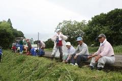 農作業姿の年配の方達が歩道の脇に腰かけている様子が写っている写真