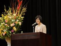 ベージュのスーツを着たタレントの高木美保さんが舞台上で話をしている写真