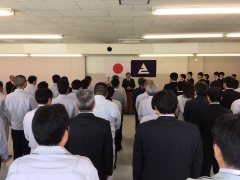 前方の日本国旗とえびの市章の前に立っている市長と前方を見て立っている大勢の方々を後方から写した写真