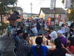 路上に飾られている提灯とその中心にテーブルが置いてあり、飲食を楽しんでいる大勢の参加者の写真