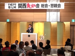 関西えびの会総会・懇親会の横断幕の下の壇上で関係者に話をしている市長の写真