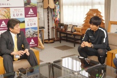 ガラステーブルがある、木目調の椅子に座っている市長と元サッカー日本代表の増田誓志選手の写真