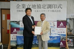 企業立地協定調印式で、市長と白いジャケットを着ている男性が一緒に協定書を持っている写真