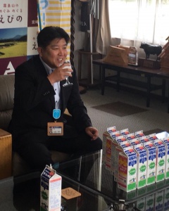 紙パックの牛乳が置いてあるガラステーブルの前に座り、 牛乳を飲んでいる市長の写真