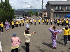 コンクリートの路上の上で、黄色いTシャツや浴衣などを着て、大きな円になり踊っている人々の写真