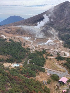 山の麓の曲がりくねった道と、ところどころで白い煙が出ている様子を上空から撮影した写真