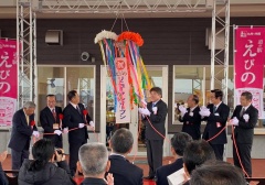 えびのと書かれた赤いのぼりが飾られ、くす玉を割って拍手している市長と関係者の方々、式典に参加されている方々を後方から写している写真
