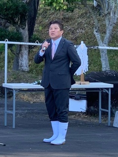 スーツ姿に白い長靴を履いている市長がマイクを持って話をしてる写真