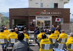 黄色いジャンパーを着た参加者やスーツ姿の関係者がパイプ椅子に座り、市長の話を聞いている様子を後方から写している開所式の写真